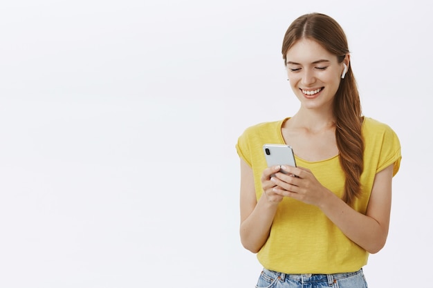 Aantrekkelijke lachende vrouw in koptelefoon luisteren muziek of podcast, met behulp van smartphone