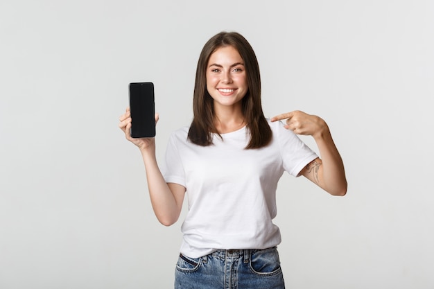 Aantrekkelijke lachende vrouw wijzende vinger op smartphonescherm, wit.