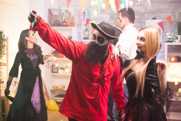 Aantrekkelijke man en vrouw verkleed als piraat en vampier die een selfie maken op halloween-feest.