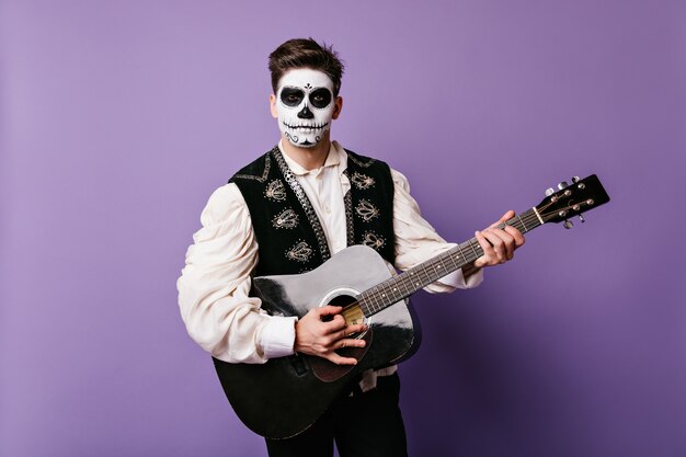 Aantrekkelijke man in outfit voor Mexicaans carnaval speelt gitaar. Close-upportret van brunet op geïsoleerde muur.