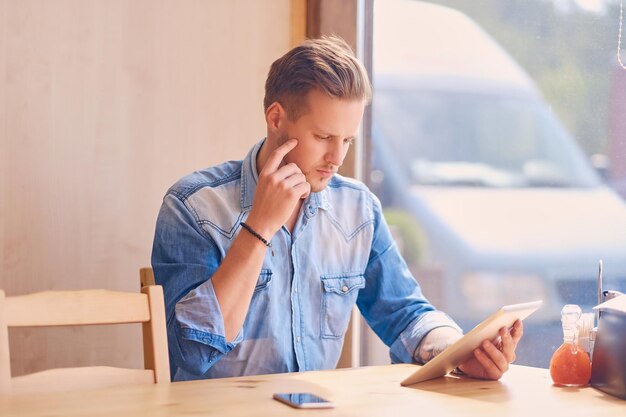 Aantrekkelijke man met behulp van een tablet-pc in een café bij het raam.