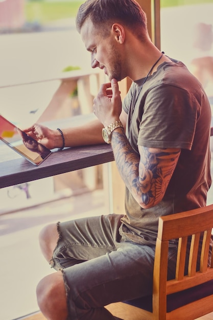 Aantrekkelijke man met behulp van een tablet-pc in een café bij het raam.