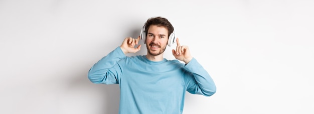Gratis foto aantrekkelijke moderne man met baard glimlachend blij met het aanraken van de hoofdtelefoon op het hoofd terwijl hij naar muziek luistert