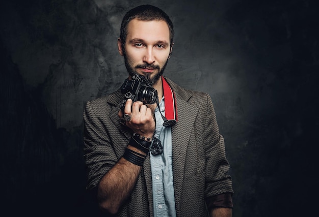 Gratis foto aantrekkelijke peinzende man met fotocamera poseert voor fotograaf in donkere fotostudio.