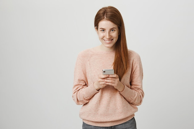 Aantrekkelijke roodharige meisje met behulp van smartphone en glimlachen