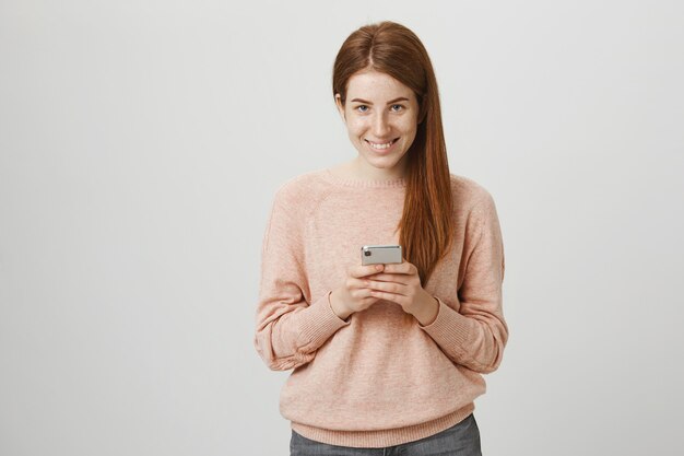 Aantrekkelijke roodharige meisje met behulp van smartphone en glimlachen