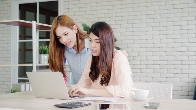 Aantrekkelijke slimme creatieve Aziatische bedrijfsvrouwen in slimme vrijetijdskleding die aan laptop terwijl het zitten werken