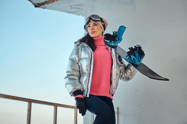 Aantrekkelijke snowboarder vrouw poseert voor fotograaf met haar snowboard.