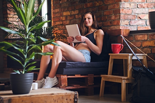 Aantrekkelijke sportieve vrouw die tablet-pc's gebruikt en koffie drinkt in de binnenkamer van de loft.