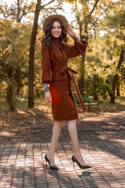 Aantrekkelijke stijlvolle lachende magere vrouw met krullend haar wandelen in het park gekleed in warme bruine vacht, herfst trendy mode Streetstyle