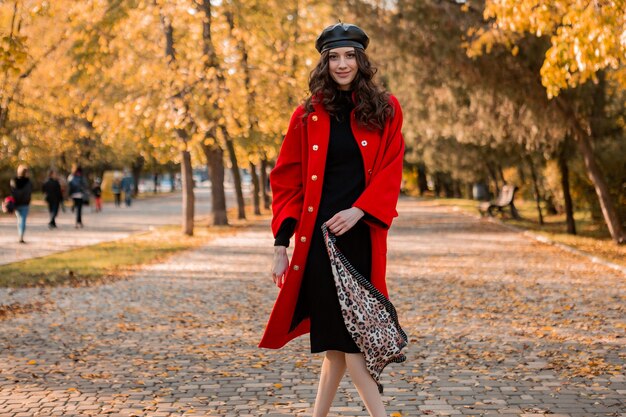 Aantrekkelijke stijlvolle lachende vrouw met krullend haar wandelen in park gekleed in warme rode jas herfst trendy mode, Streetstyle, baret hoed en luipaard gedrukte sjaal dragen