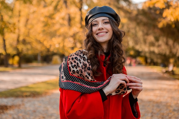 Aantrekkelijke stijlvolle lachende vrouw met krullend haar wandelen in park gekleed in warme rode jas herfst trendy mode, Streetstyle, baret hoed en luipaard gedrukte sjaal dragen