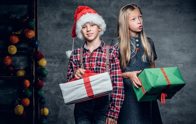 Aantrekkelijke tiener op kerstmuts en schattig blond meisje houdt kerstcadeaudozen vast.