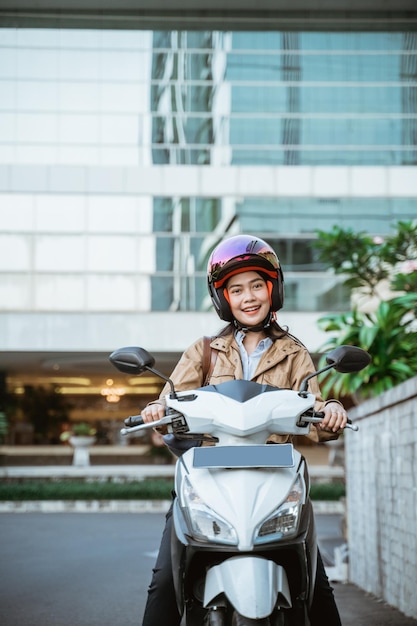 Aantrekkelijke vrouw die een helm draagt tijdens het rijden op een motorfiets tegen de achtergrond van een gebouw Premium Foto