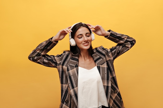 Aantrekkelijke vrouw in wit T-shirt, oversized jas lacht breed en draagt een koptelefoon