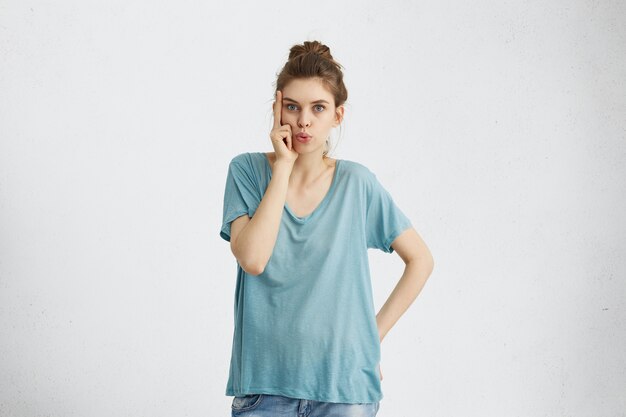 Aantrekkelijke vrouw met blauwe warme ogen, gekleed in losse blauwe casual T-shirt iets schaven terwijl haar vingers op tempels.