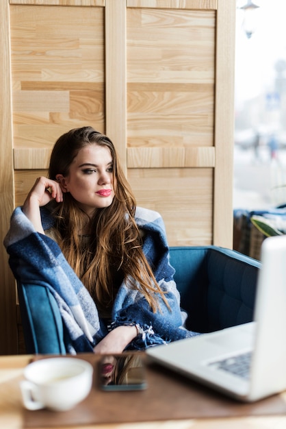 Gratis foto aantrekkelijke vrouw met deken op zoek naar haar laptop