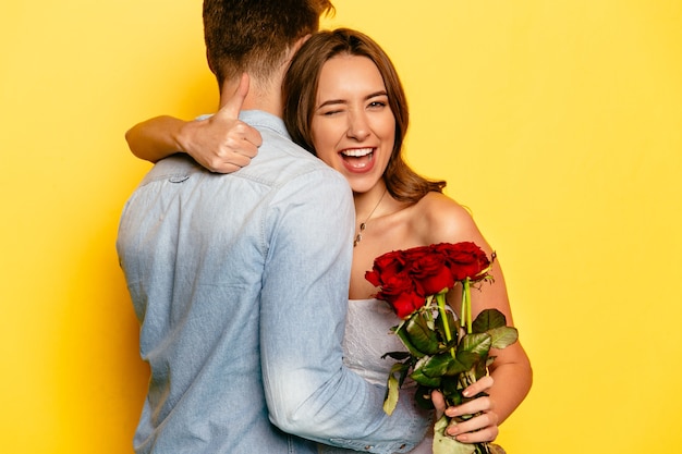 Aantrekkelijke vrouw met rode rozen die en een duim knipogen tonen terwijl het koesteren van haar vriend.