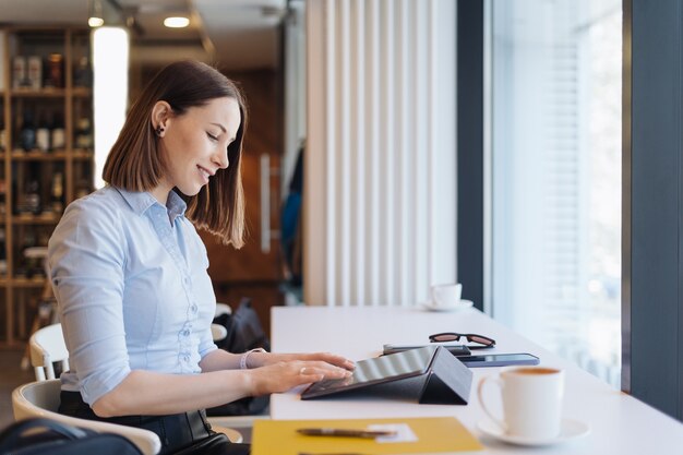 Aantrekkelijke vrouw met schattige glimlach met een kopje koffie terwijl relaxin in een pauze met een digitale tablet