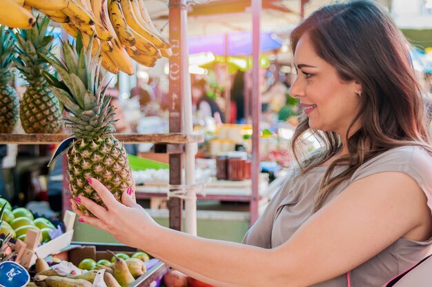 Aantrekkelijke vrouw winkelen in de groene markt. Close-up portret mooie jonge vrouw op te halen, kiezen van vruchten, ananas. Positieve gezichtsuitdrukking emotie voelen gezonde levensstijl