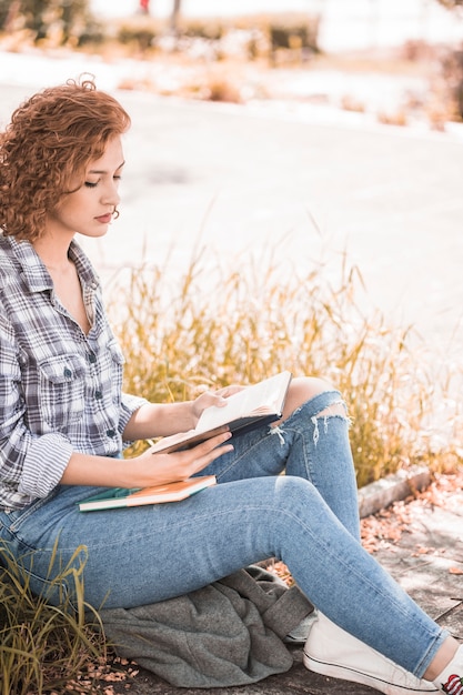 Aantrekkelijke vrouw zittend op het gras en het lezen van boek