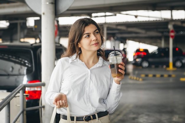 Aantrekkelijke zaken jonge vrouw in een parkeergarage met een kopje koffie