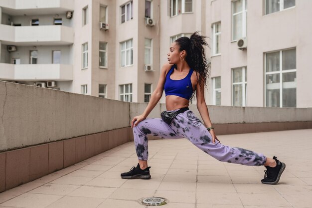 Aantrekkelijke zwarte afro-amerikaanse vrouw in sportfitness-outfit op het dak om te trainen