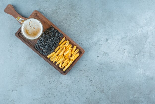 Aardappelfrietjes, zonnebloempitten en een glas bier aan boord op blauw.