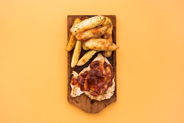 Aardappelpartjes en vlees met saus op een houten bord