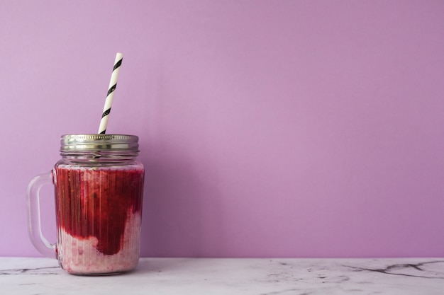 Aardbei smoothie in pot met gesloten deksel en rietje tegen roze achtergrond