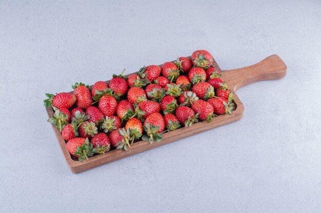 Aardbeien gerangschikt op een houten bord op marmeren achtergrond.