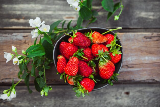 Aardbeien in een kom met bloem tak bovenaanzicht op oude houten tafel