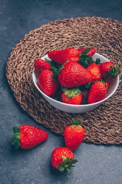 Aardbeien in een mening van de kom hoge hoek over een onderzetter en een grijze geweven achtergrond