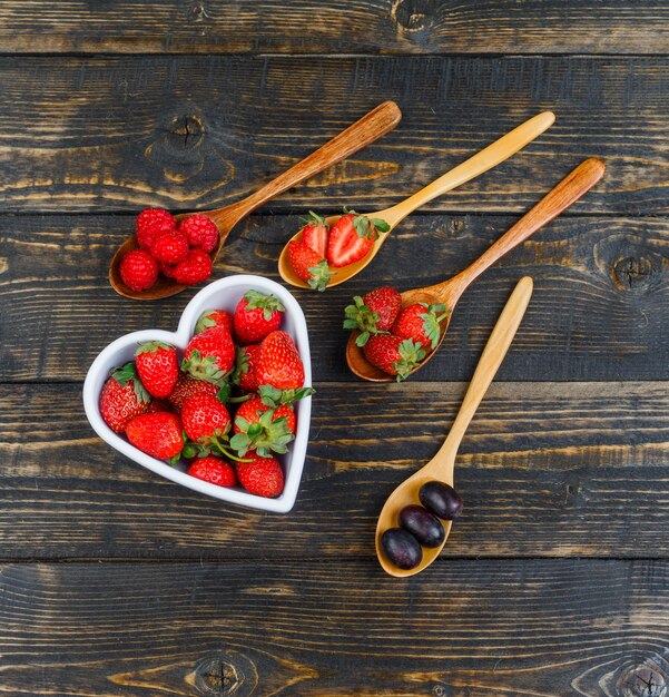 Aardbeien in kom met fruit op houten lepel