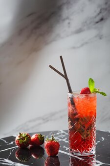 Aardbeienmojito met muntblad op marmeren tafel. verse dranken met aardbei en tropische tak op de achtergrond.