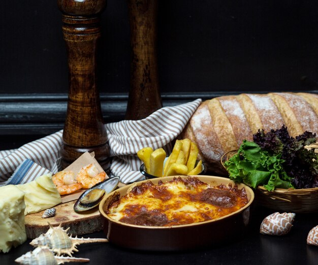 Aardewerken pan met schotel bedekt met gesmolten kaas, geserveerd met garnalen en mossel
