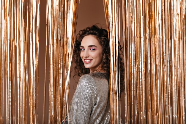 Aardige dame in zilveren outfit lachend op gouden achtergrond