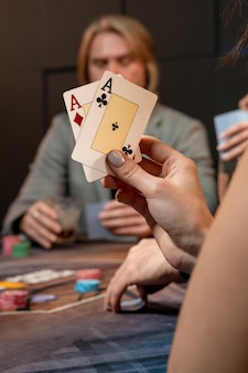 Aas van diamanten en aas van clubs in de hand van jonge vrouw zittend aan speeltafel met gokfiches in gokinrichting en poker spelen op onscherpe achtergrond van spelers, bijgesneden schot