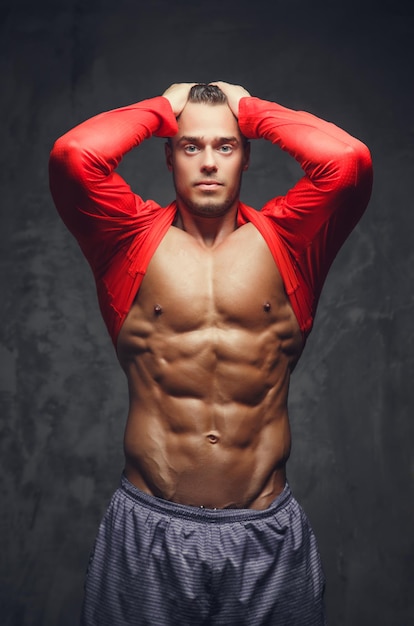 Abdominale bodybuilder model in een rode trui poseren in een studio op grijze achtergrond.