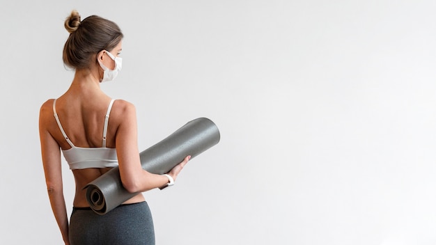 Gratis foto achter mening van vrouw met medisch de yogamat van de maskerholding