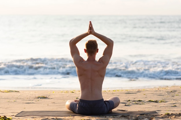 Gratis foto achteraanzicht man doet yoga op het strand buiten