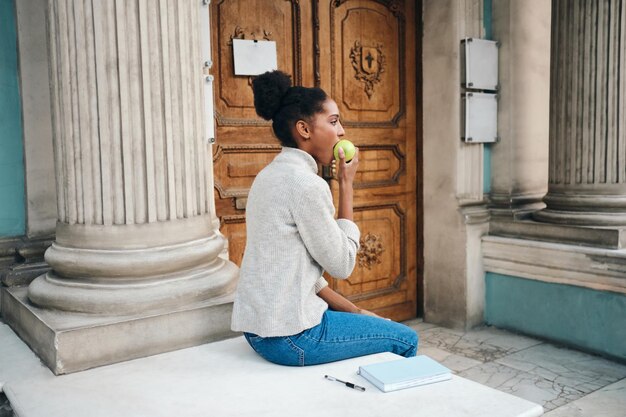 Achteraanzicht van aantrekkelijk Afro-Amerikaans meisje in trui die appel eet op straat in de stad