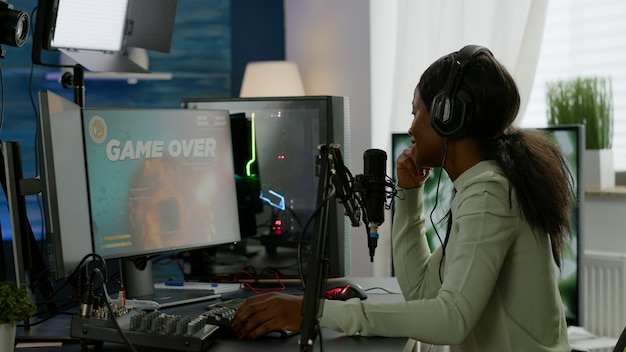 Achteraanzicht van afro-amerikaanse esport-streaming die virtuele concurrentie met een koptelefoon verliest. Professionele gamer die online videogames streamt met nieuwe graphics op een krachtige computer.