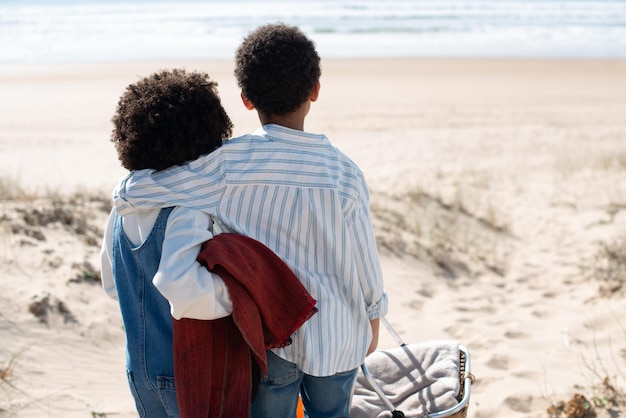 Achteraanzicht van Afro-Amerikaanse kinderen op het strand. Broer en zus in vrijetijdskleding kijken naar water, knuffelen. Portret, familie, kinderconcept