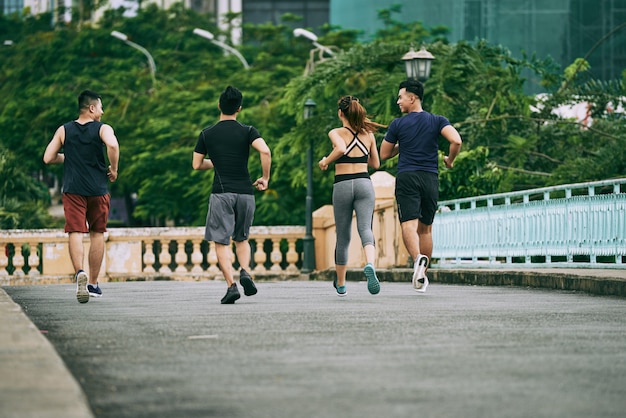 Achteraanzicht van drie man en een meisje joggen samen op een zomerdag