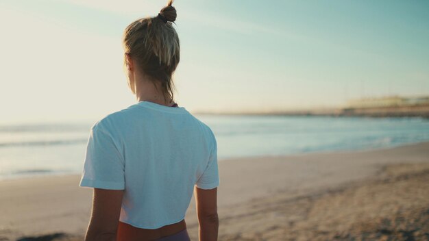 Achteraanzicht van een blonde vrouw die geniet van een goede dag na yogabeoefening op het strand Sportief meisje dat aan zee staat