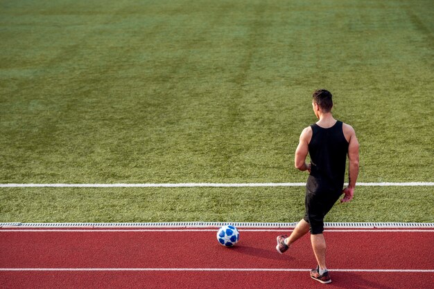 Achteraanzicht van een sporter spelen op racebaan met voetbal