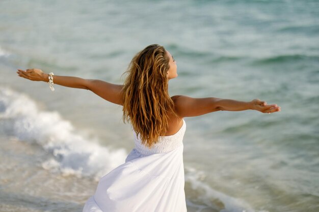 Achteraanzicht van een vrouw die zich vrij voelt terwijl ze bij de zee staat met haar armen uitgestrekt