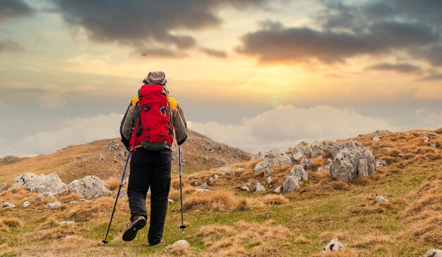 Achteraanzicht van een wandelaar die vanaf een berg naar de zonsondergang kijkt