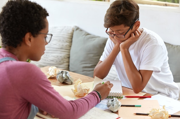 Achteraanzicht van ervaren Afro-vrouw legt de inhoud van het schoolonderwijs uit aan mannelijke hipster